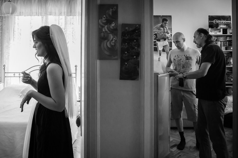 Bride getting ready in one room while groom and father in other room